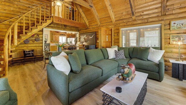 Ein gemütliches Blockhaus-Interieur mit einem grünen Sofa, einer Holztreppe und rustikalen Einrichtungsgegenständen.