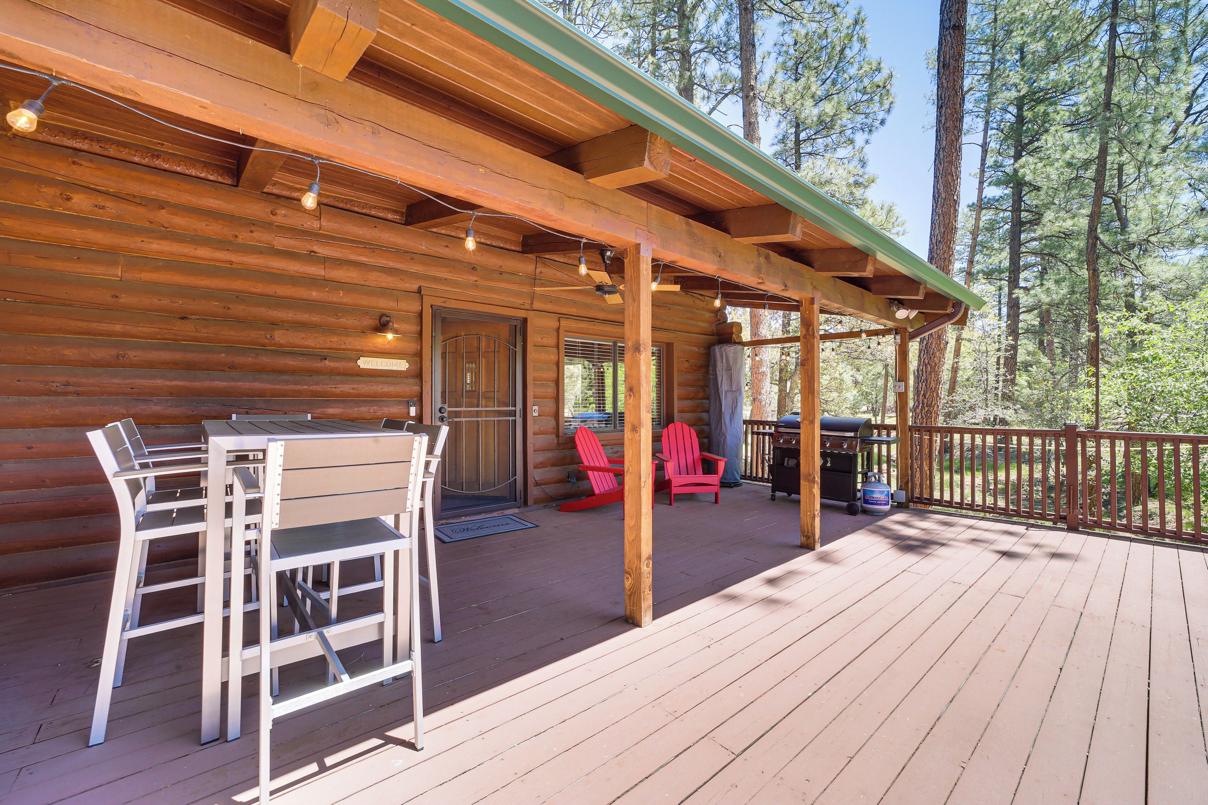 A wooden cabin with a covered deck, outdoor seating, and a grill area.