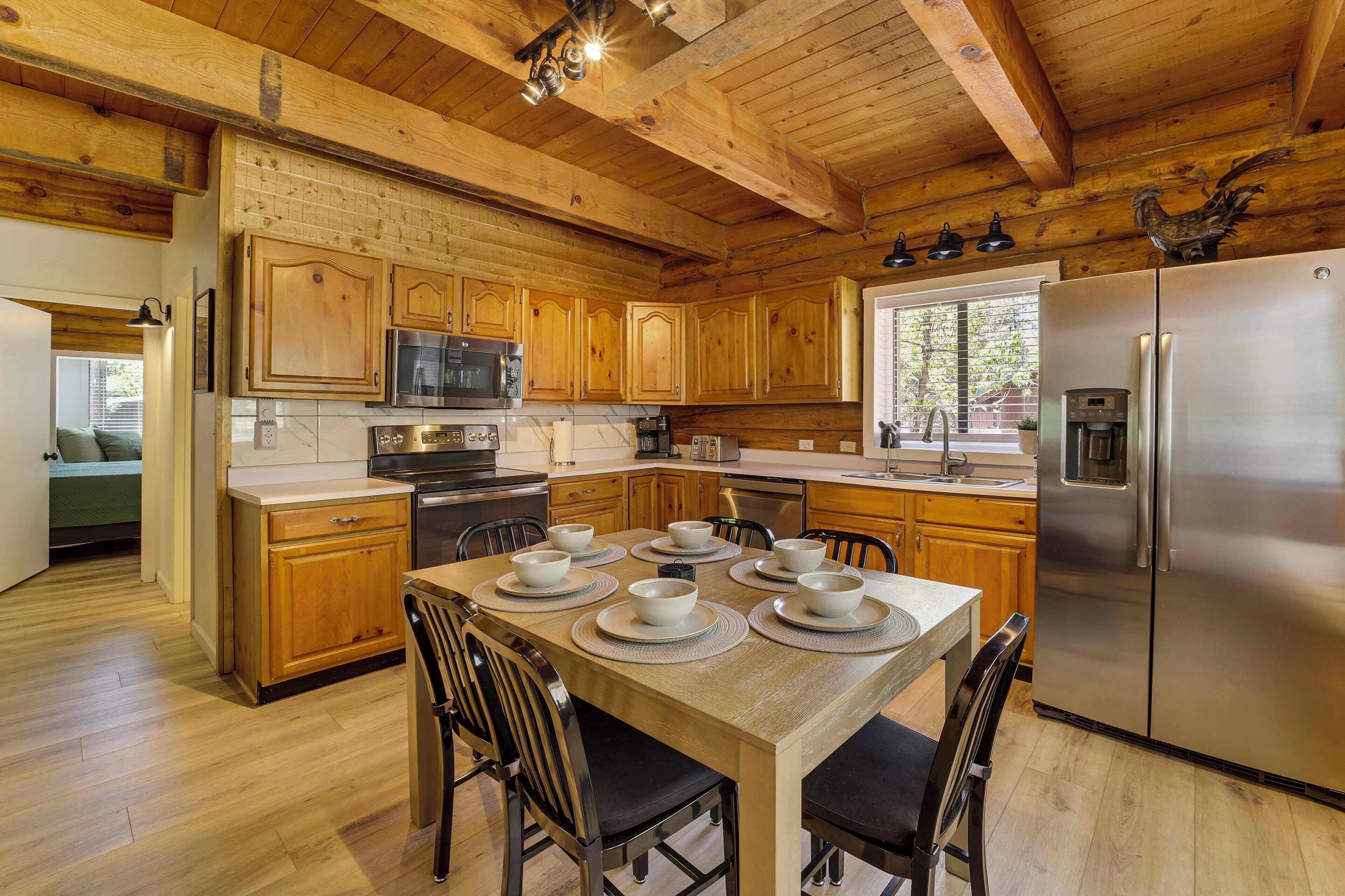 A wooden cabin-style kitchen with a dining table set for six, stainless steel appliances, and a large window.