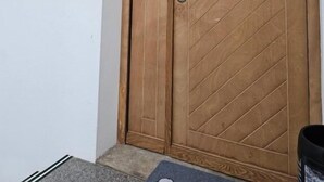 Une porte à deux battants en bois, dotée d’un trou de serrure et d’une poignée ronde, encastrée dans un mur blanc, avec une petite marche menant à son seuil.