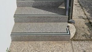 Un escalier en pierre, agrémenté de rampes métalliques, mène à l’entrée d’un bâtiment.