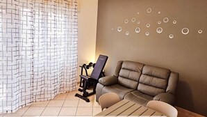 Une pièce avec un canapé gris, un vélo d’appartement noir et un rideau à motifs.