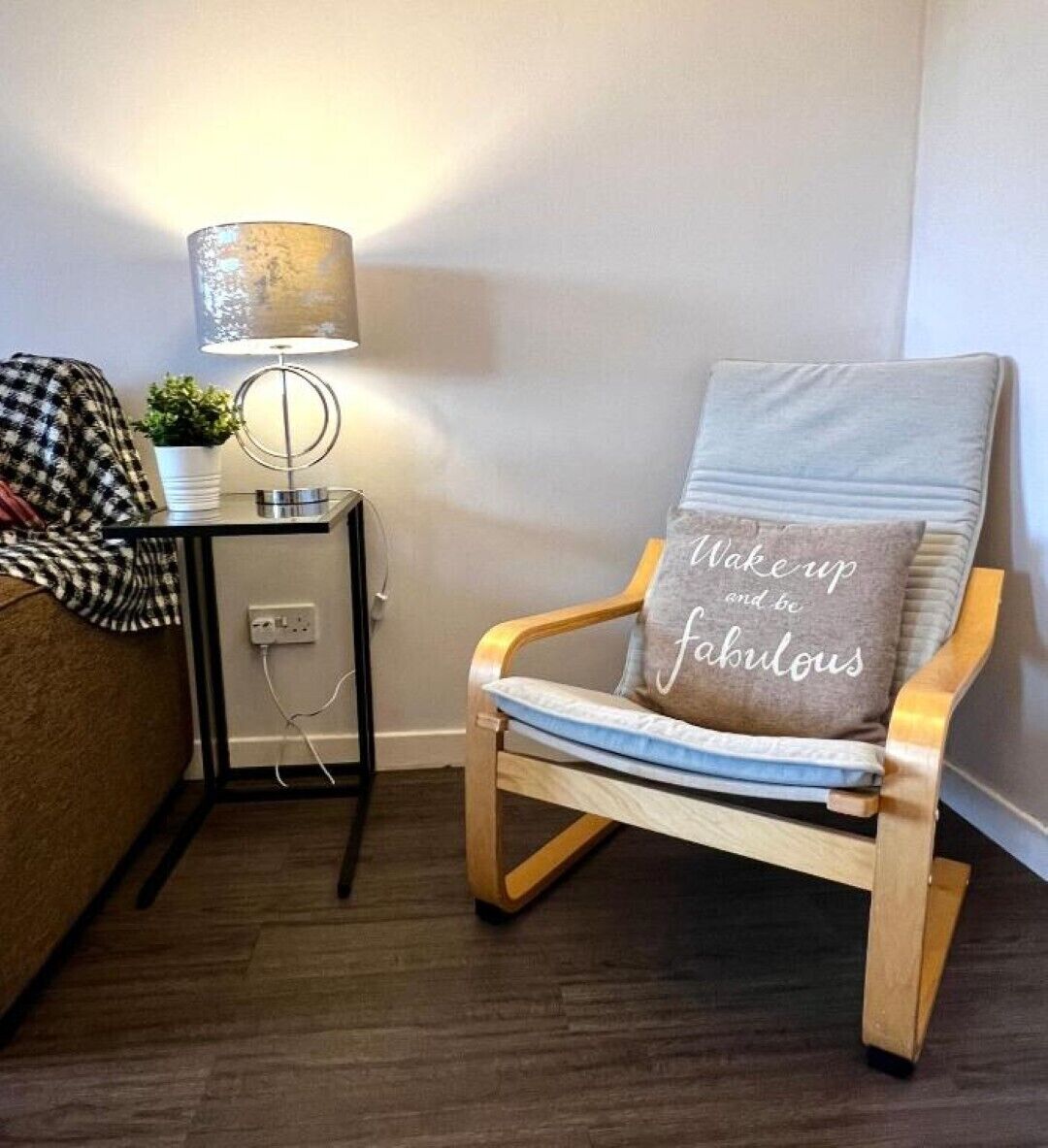 A modern room with a wooden armchair, a small side table with a lamp, and a cushion with motivational text.