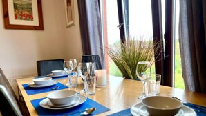 Une table à manger dressée avec des assiettes, des verres et des couverts, et une vue sur la verdure par la fenêtre.