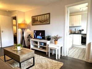 Un salon avec un téléviseur, une table basse, une bibliothèque et un tableau accroché au mur.