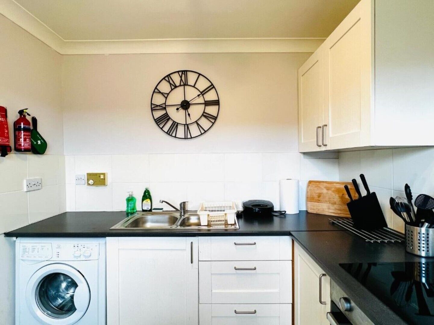 Una cocina compacta con lavadora, un lavabo, un reloj y armarios.