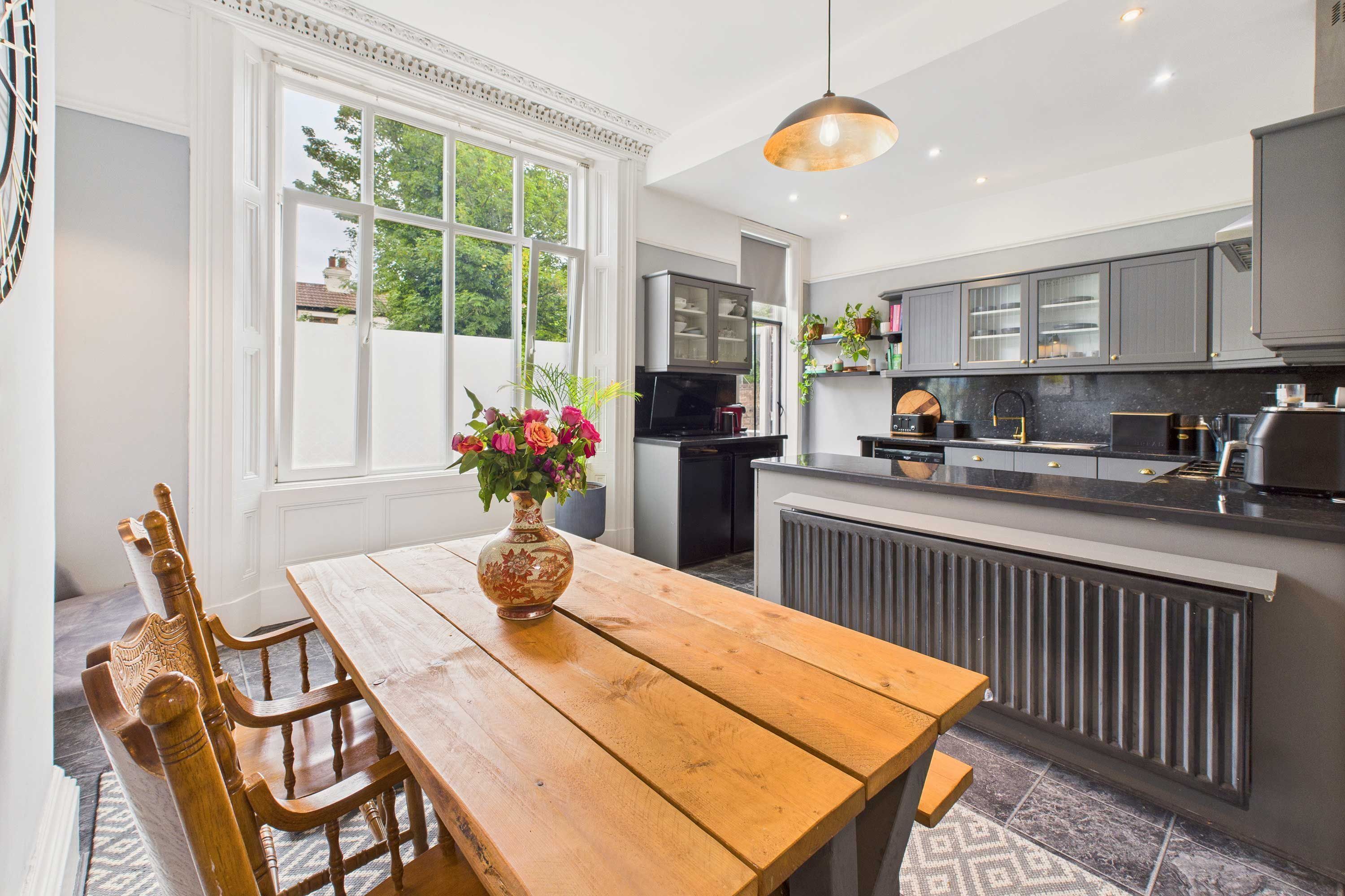 A modern kitchen with a wooden dining table, a vase of flowers, and a large window.