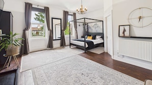 A bedroom with a four-poster bed, a chandelier, a large window with curtains, a radiator, and a plant. - Host Stay Beech Street (Liverpool)