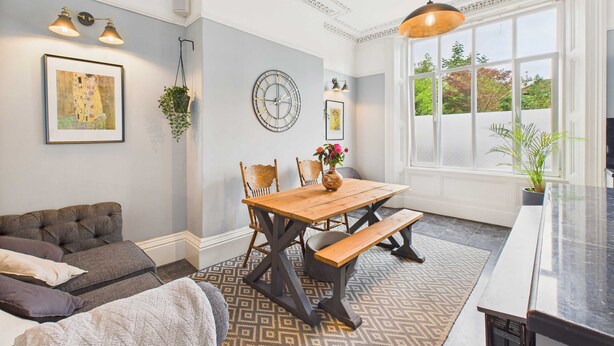A dining area with a wooden table and benches, a clock on the wall, and a large window with a view. - Host Stay Beech Street (Liverpool)