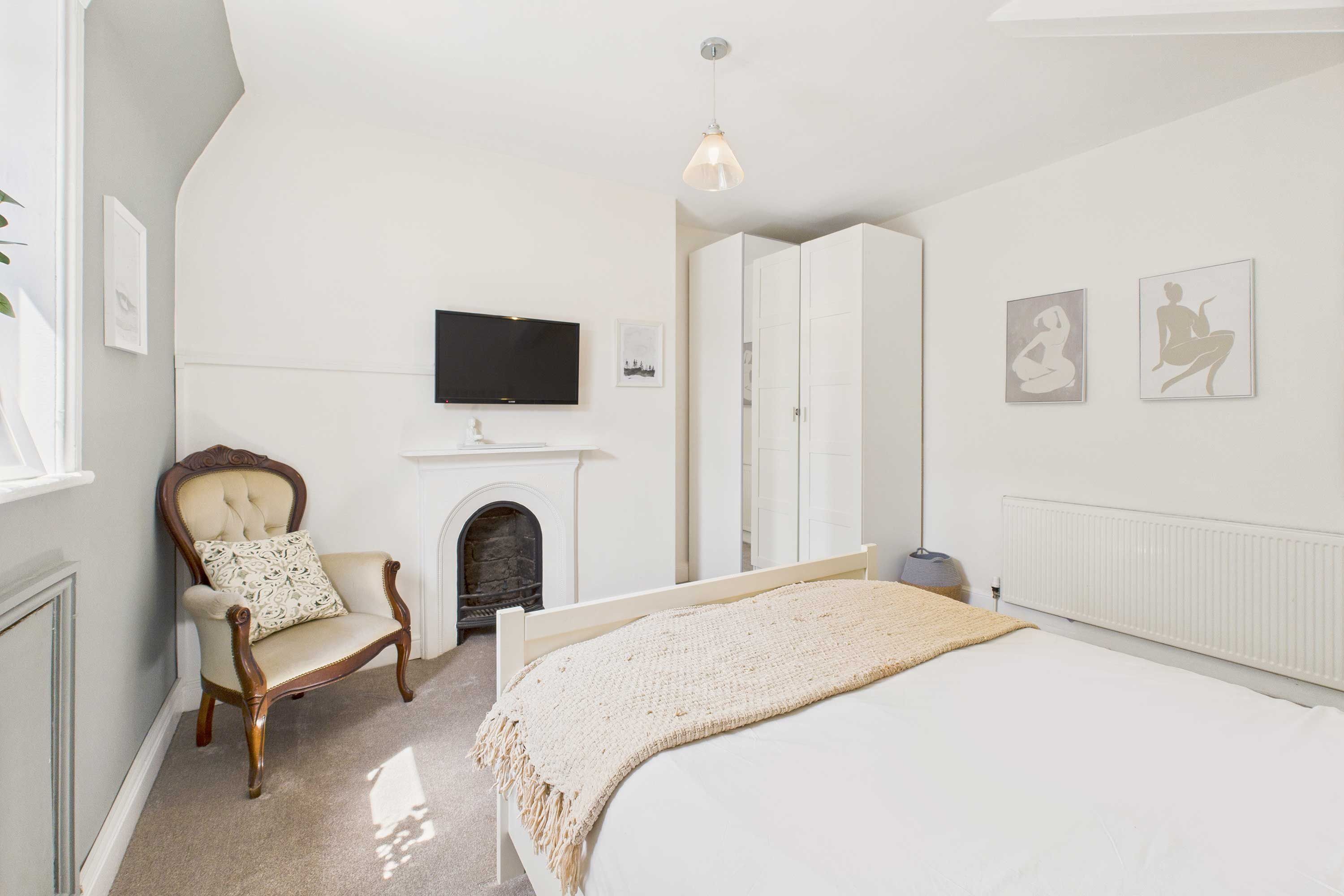 Ein Schlafzimmer mit Bett, Sessel, Kamin, Fernseher und Kunstwerken an den Wänden.