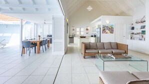 A spacious living area with a glass coffee table, a sofa, and a dining area with chairs and a table. - Ocean Whisper Villa in Sint Willibrordus (St. Marie)