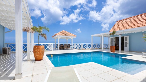 A pool area with a clear blue sky, white pergolas, and a tiled deck. - Ocean Whisper Villa in Sint Willibrordus (St. Marie)
