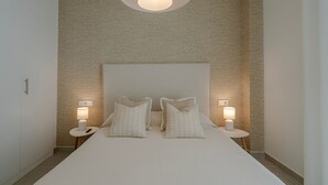 A neatly arranged bedroom with a large bed, two bedside tables with lamps, and a textured wall. - Chic Coastal Living on the New Golden Mile (Estepona)