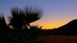La silhouette d’un palmier se détachant sur le ciel au coucher du soleil, une piscine et une montagne lointaine.