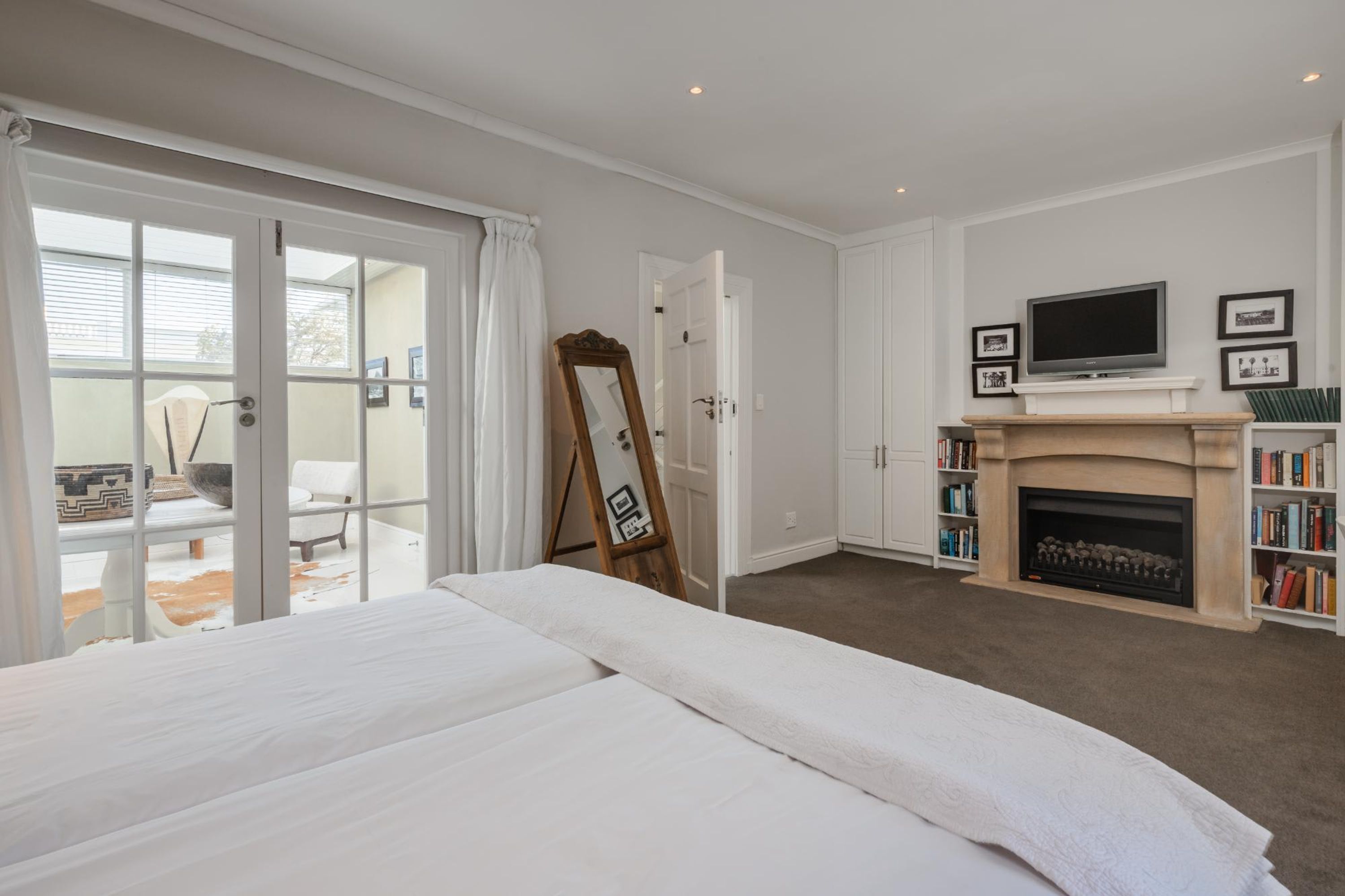 A bedroom with a large bed, a fireplace, a television, and a sliding glass door leading to a balcony.