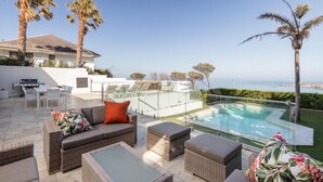 Une terrasse avec des meubles en osier, une table en verre et une piscine.