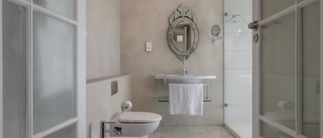 A bathroom with two toilets, a sink, a mirror, and a glass shower enclosure.