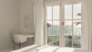 Une chambre avec une grande fenêtre, un lit, une chaise et un miroir rond accroché au mur.