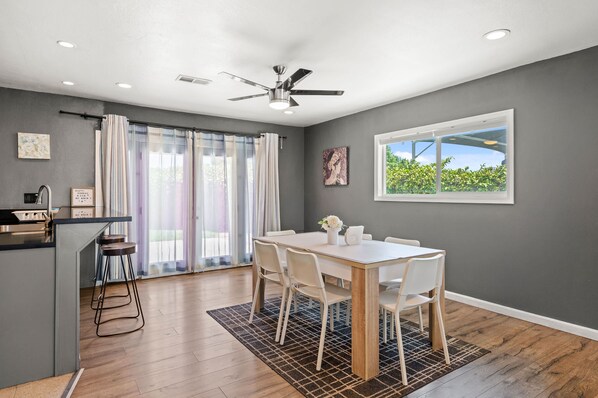 A modern kitchen with a bar area, a dining table with chairs, and a ceiling fan.