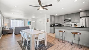 A modern kitchen with grey cabinets, a stainless steel refrigerator, and a microwave. There is a dining area with a white table and chairs, and a ceiling fan above. - Spacious Family Friendly House in Central Location (La Puente)