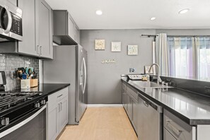 A modern kitchen with grey cabinets, stainless steel appliances, and a tiled backsplash. - Spacious Family Friendly House in Central Location (La Puente)