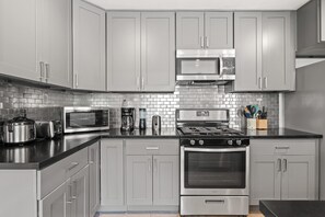 A modern kitchen with grey cabinets, a stainless steel stove, a microwave, and a coffee maker. - Spacious Family Friendly House in Central Location (La Puente)