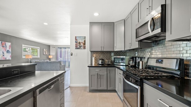 A modern kitchen with grey cabinets, a black countertop, and stainless steel appliances. - Spacious Family Friendly House in Central Location (La Puente)