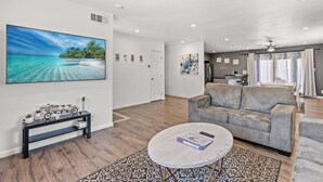 A spacious living room with a large flat-screen TV, a grey sofa, a coffee table, and a patterned rug. - Spacious Family Friendly House in Central Location (La Puente)