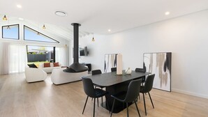 A modern living room with a fireplace, a dining area with a large table and chairs, and a view of the outdoors. - 13A Alice Street, Jindabyne (Jindabyne)