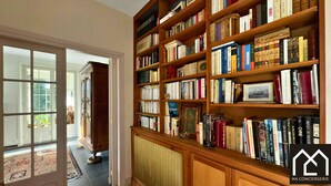 Eine Bibliothek mit hölzernen Bücherregalen, gefüllt mit Büchern, einem Heizkörper und einer Tür zu einem anderen Raum.
