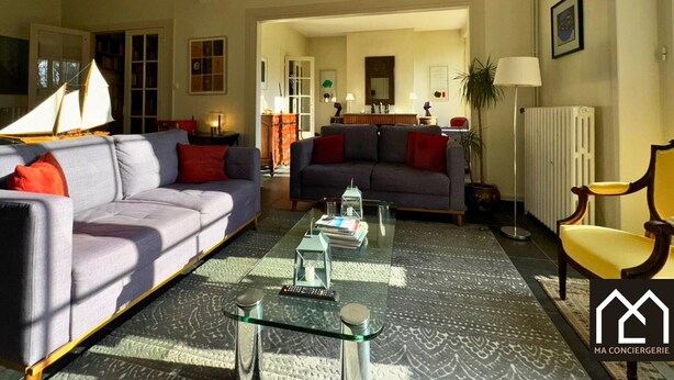 Ein Wohnzimmer mit einer Couch, einem Sessel und einem Couchtisch mit Büchern und einem Schiffmodell.