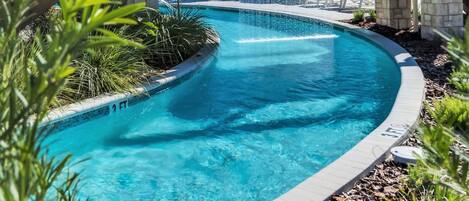 A swimming pool with a wooden bridge, lounge chairs, and palm trees.