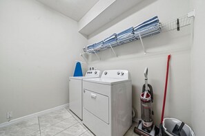 A laundry room with a washing machine, dryer, and stacked laundry on a rack.