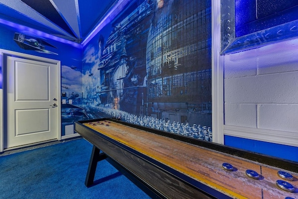 A room with a shuffleboard table, a door, and a wall mural.