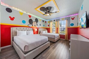 Habitación de hotel con dos camas, ventilador de techo y decoración de paredes con temática de Mickey Mouse.