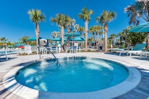 Un área de piscina con una piscina circular, sillas de descanso, palmeras y sombrillas.