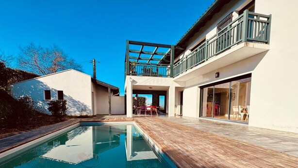 A modern house with a swimming pool, a covered patio, and a balcony with a view.