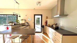 A modern kitchen with a large window, wooden flooring, and a dining area with stools.