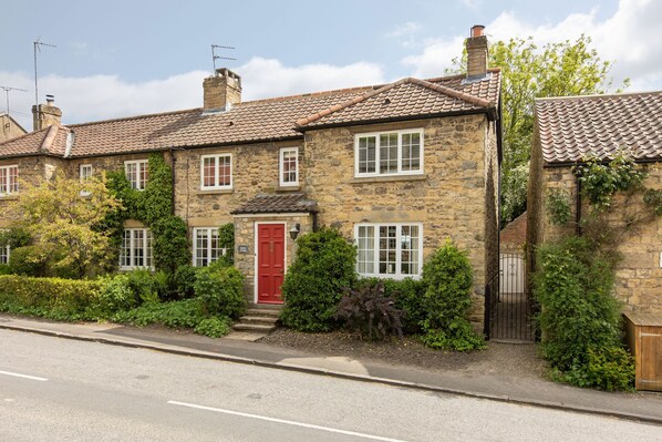 A stone house with a red door, multiple windows, and a garden.