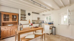 Una cocina con armarios de madera, una mesa de comedor con bancos, un cesto de basura y una ventana con vistas al verdor.