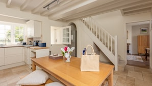 Cocina amplia con una mesa de madera, un banco y un jarrón de flores. Una escalera conduce a otra habitación.