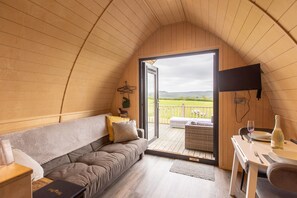 Een gezellige kamer met houten lambrisering, een bank, een eettafel en een aan de muur bevestigde televisie.