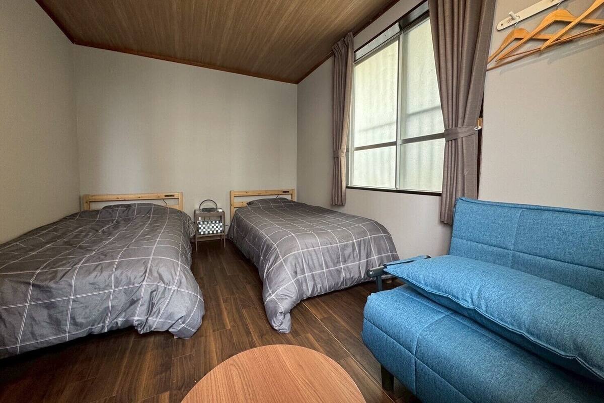 Una habitación con dos camas, un sofá azul y una ventana con cortinas.