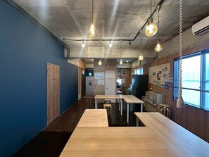 A modern interior with a long wooden table, hanging pendant lights, and a view of the sea through large windows.