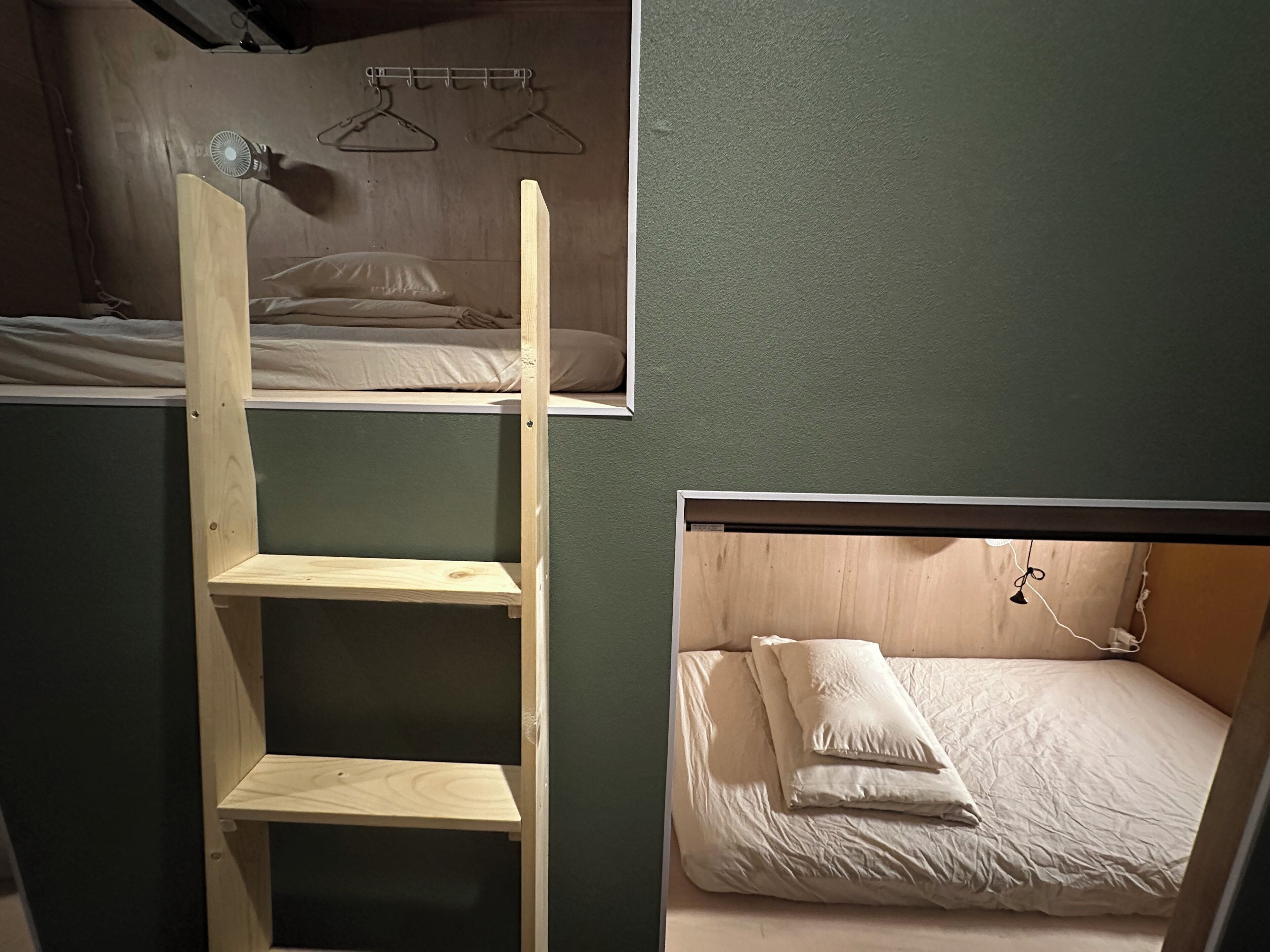 A dormitory room with bunk beds, a wooden ladder, and a small shelf.