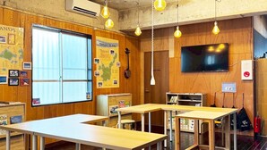 Een klaslokaal met houten wanden, een groot raam en een televisie. Tafels en krukken staan klaar voor zittende leerlingen.