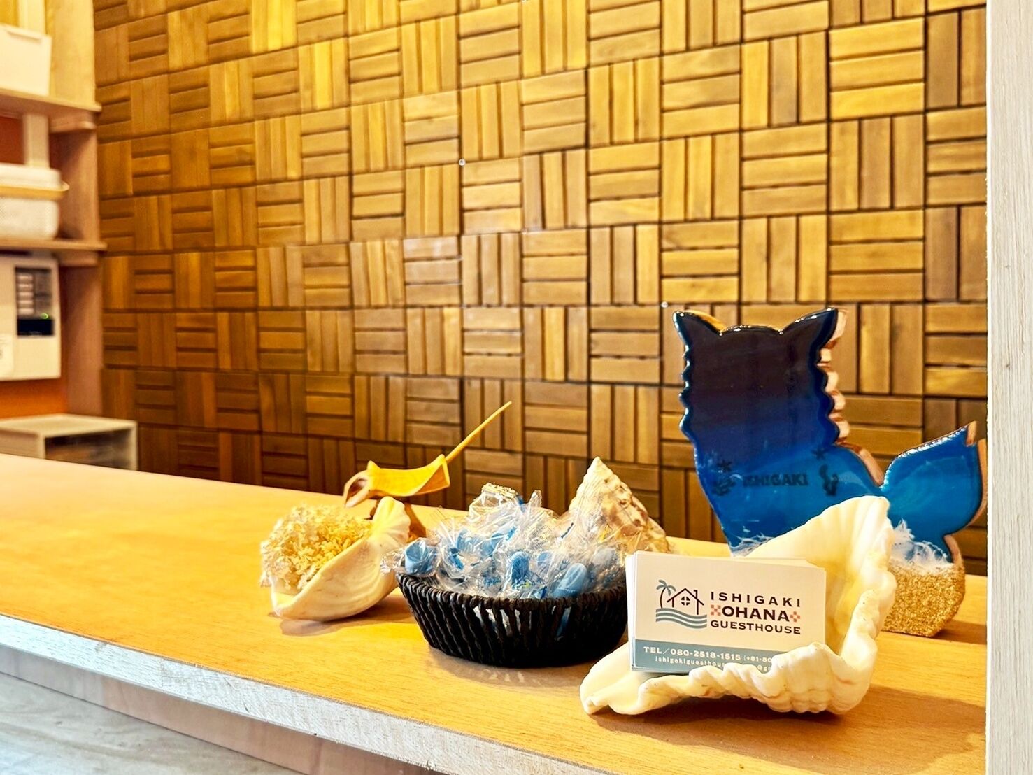 A reception area with a wooden wall, a counter with a business card, a decorative bowl, and a blue ceramic piece.