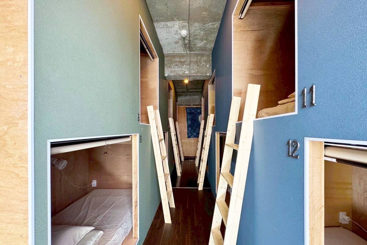 Un pasillo estrecho con literas a ambos lados, escaleras de madera y una pared azul con un letrero con el número '12'.
