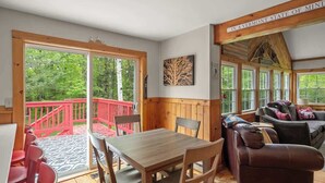Ein Zimmer mit Holztisch und -stühlen, einer Couch und einer roten Terrasse, die nach draußen führt.