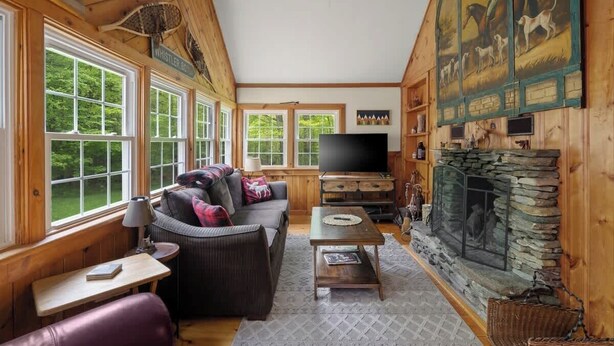 Ein gemütliches Blockhauss-Interieur mit Kamin, Holzwänden, einem großen Fernseher und einer Couch.